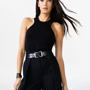 Woman wearing a black sleeveless top and high-waisted pants with a belt on a white background