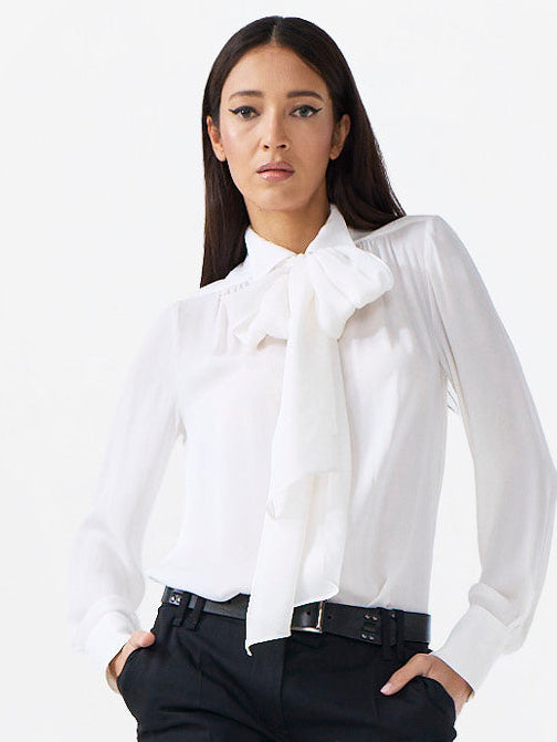 Woman wearing a white blouse with a bow tie and black pants on a white background